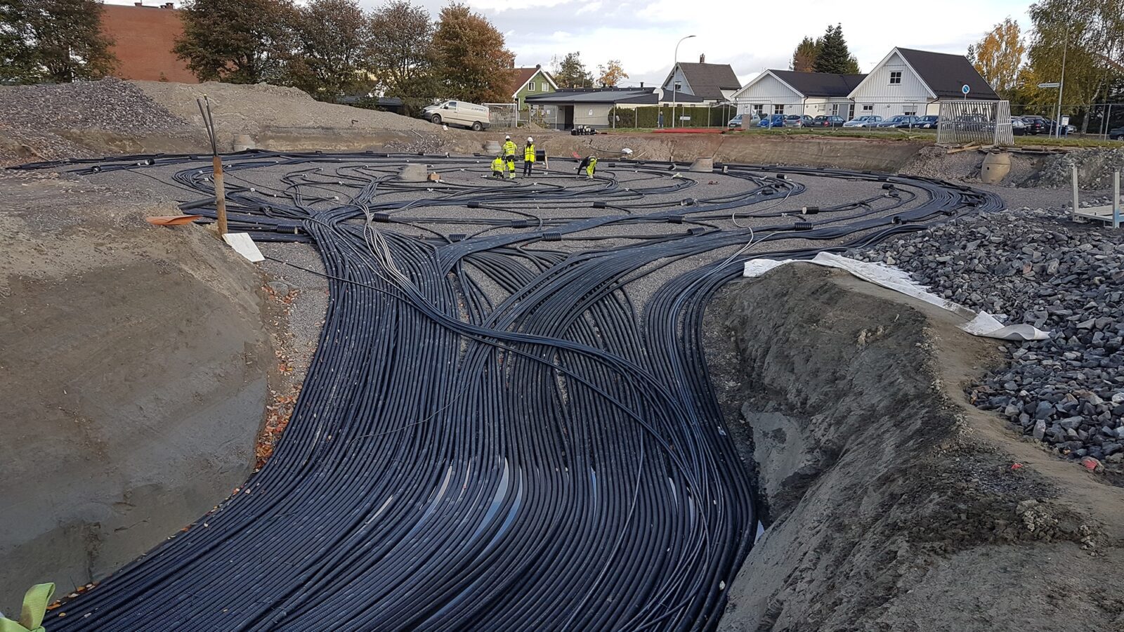 Arbeidere i gule jakker som jobber med et ledningsnett som skal graves ned i jorda ved et boligfelt.