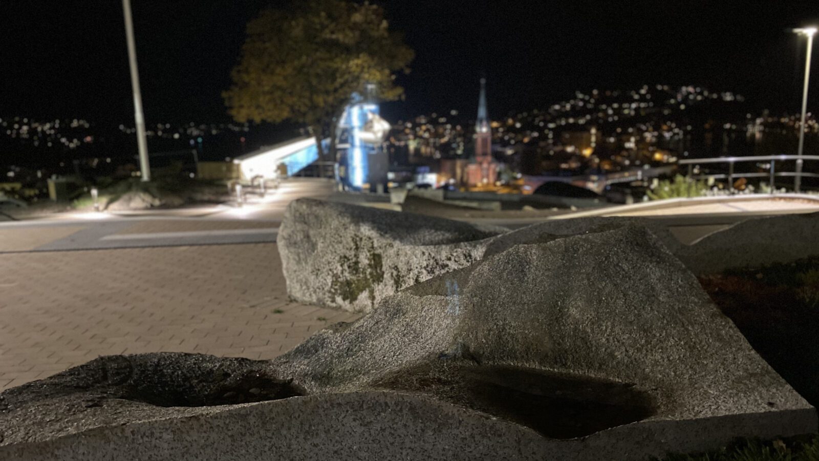 Kveldsbilde i mørket av svaberg med lyng på toppen av Fløyheia, med utsikt over byen i bakgrunnen